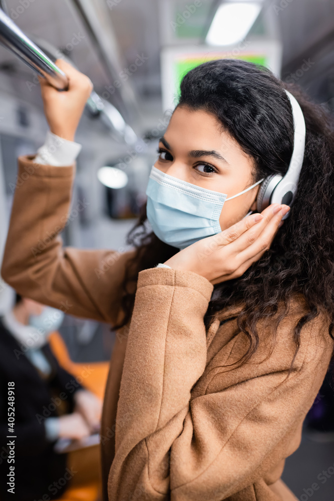 curly african american woman in medical mask listening music in subway