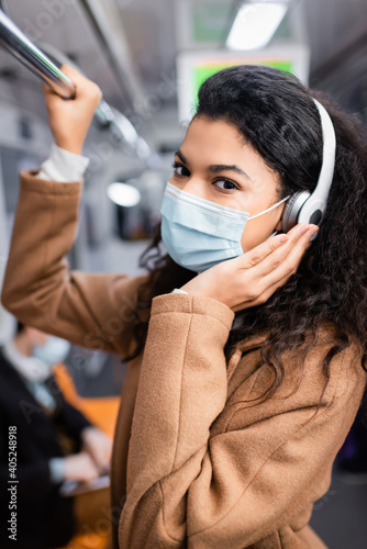 curly african american woman in medical mask listening music in subway