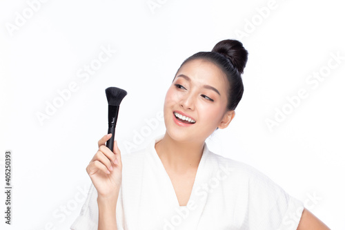Closeup portrait of beautiful happy young girl holding brush near face isolated on white background. Beauty and cosmetics concept.