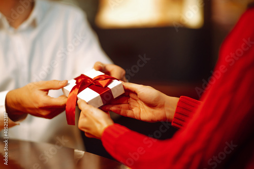 Exchange of gifts. Man gives to his woman surprise a gift box with red ribbon.Young loving couple celebrating Valentines Day. Romantic day. Winter holidays.