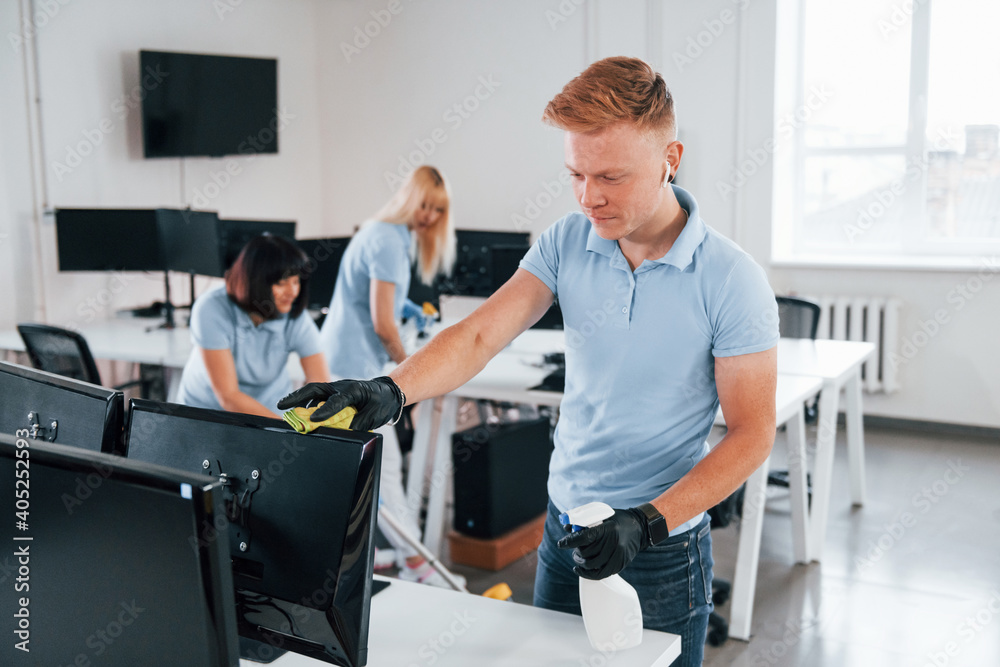 Cleans monitor. Group of workers clean modern office together at daytime Cleans monitor. Group of workers clean modern office together at daytime