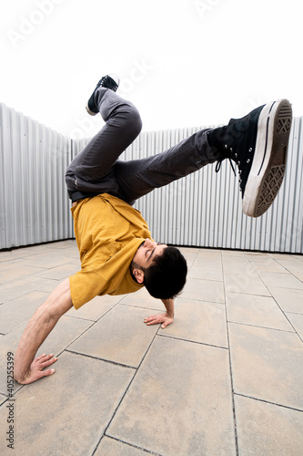 Caucasian white guy with beard dancing break dance underground hip hop with gray sweatshirt and metallic gray background deadly acrobatics flexibility