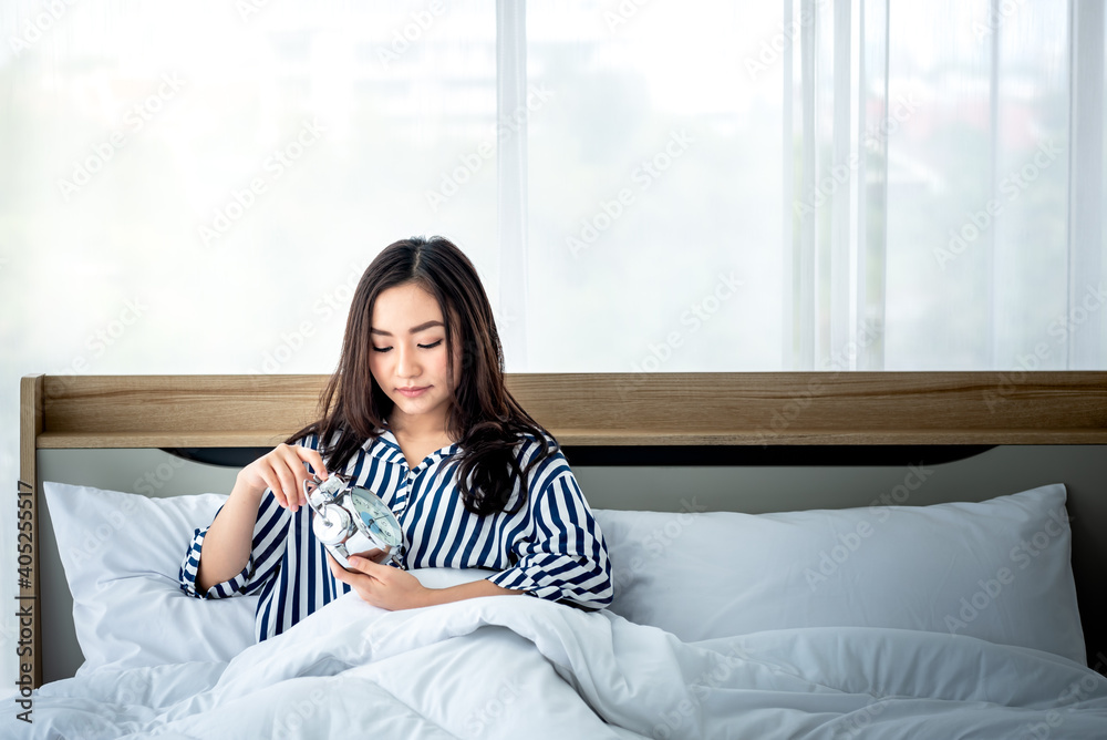 portrait images of Asian attractive woman on white bed in bedroom Using the alarm clock to set the time For waking her asleep, to people and bedroom concept.