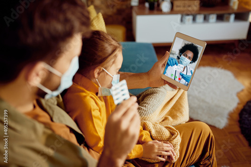 Close-up of father with ill daughter consulting a doctor via video call about prescription medicines during coronavirus pandemic.