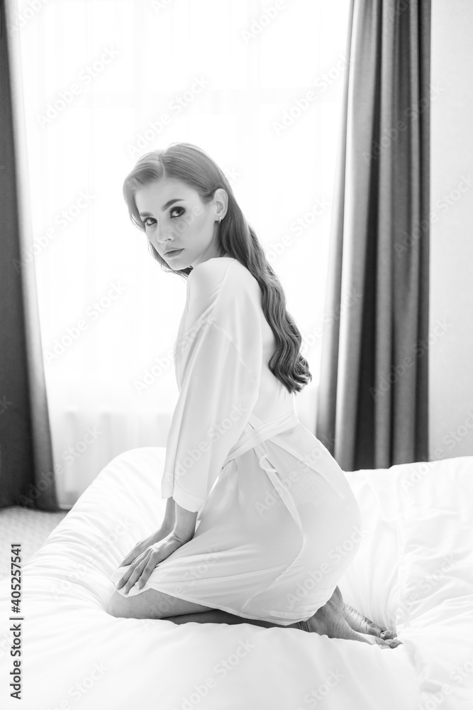 black and white.beautiful woman with makeup, long hair sits in white robe on bed black and white.beautiful woman with makeup, long hair sits in white robe on bed