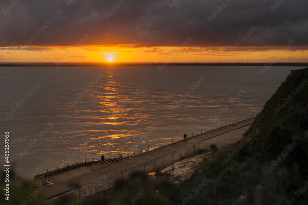 A break in heavy clouds allows for a beautiful sunset in Ramsgate, Kent, UK. People are watching from a low level promenade. A break in heavy clouds allows for a beautiful sunset in Ramsgate, Kent, UK. People are watching from a low level promenade.