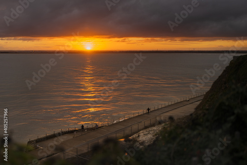 A break in heavy clouds allows for a beautiful sunset in Ramsgate, Kent, UK. People are watching from a low level promenade.