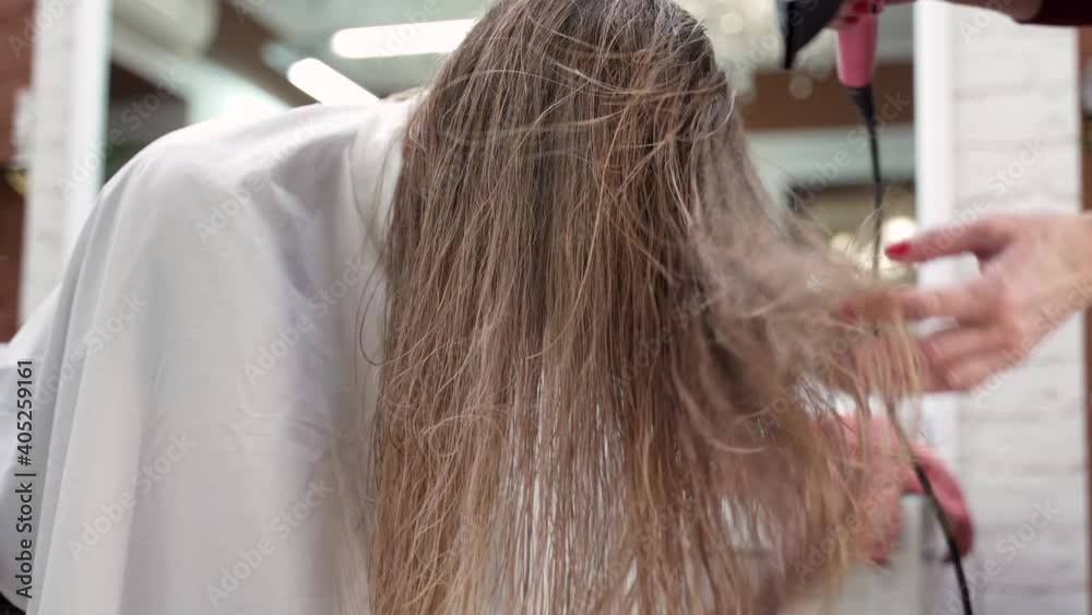 hairdresser's hands blow dry the girl's long blonde hair with her head down hairdresser's hands blow dry the girl's long blonde hair with her head down