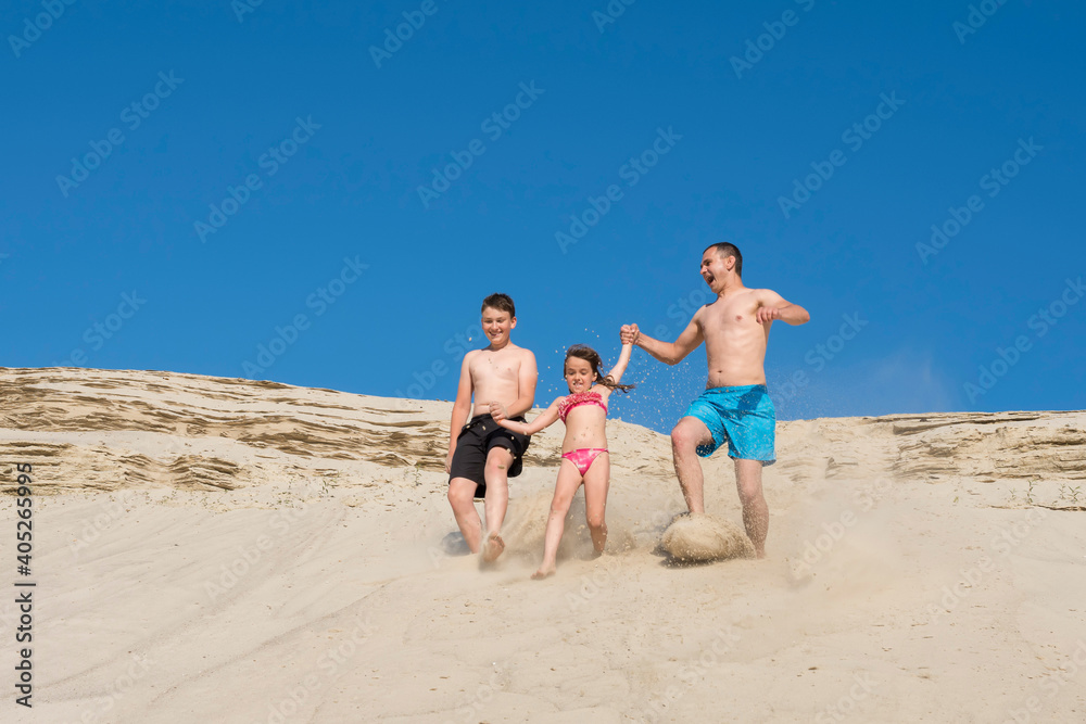 Happy children with their father run on the sand on the beach. Family on summer vacation, Sports games, sports, vacation, lifestyle