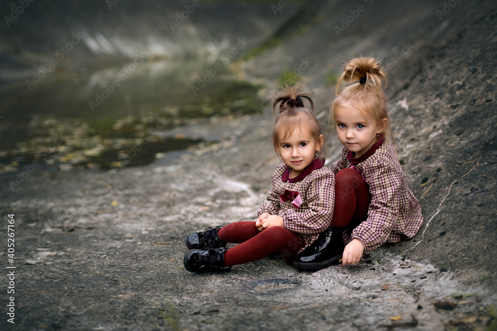 Two little friends dressed the same sitting on the rocks and looking into the camera Two little friends dressed the same sitting on the rocks and looking into the camera