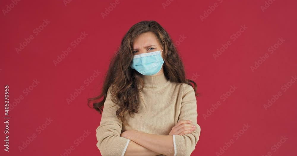 Studio woman portrait on red background offended caucasian millennial woman teenager girl in sweater with long hair beautiful model wears medical protective face mask folds arms crossed gesture angry Studio woman portrait on red background offended caucasian millennial woman teenager girl in sweater with long hair beautiful model wears medical protective face mask folds arms crossed gesture angry