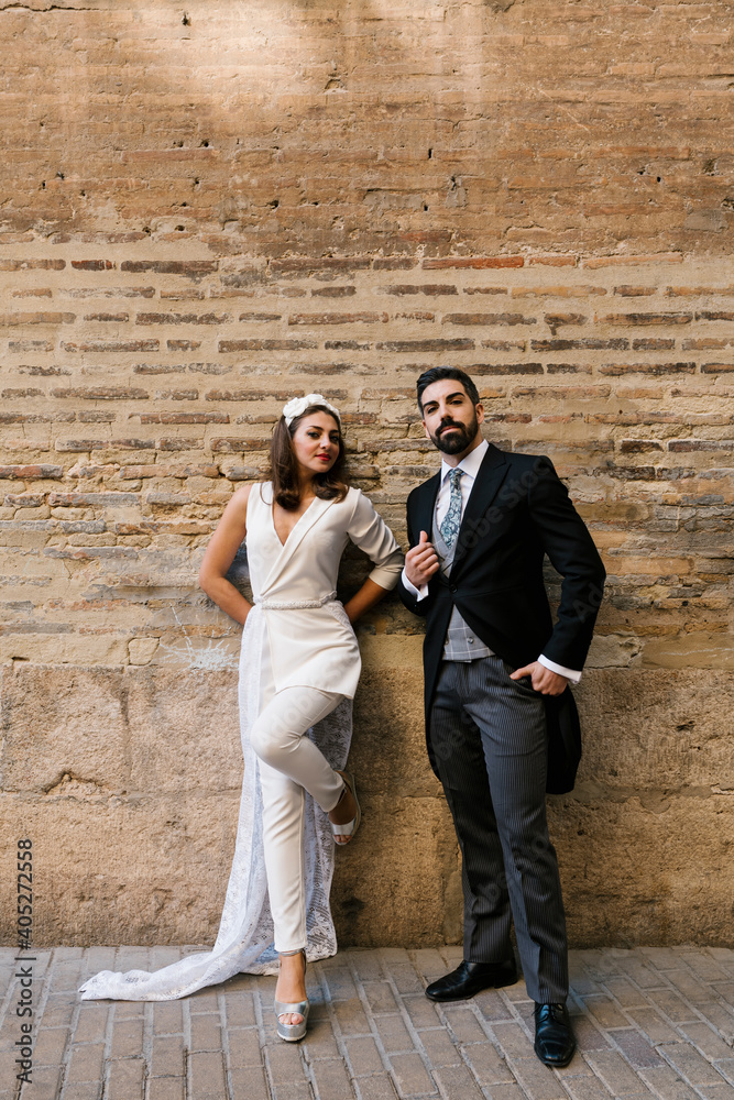 Young newly married couple standing against wall on footpath Young newly married couple standing against wall on footpath