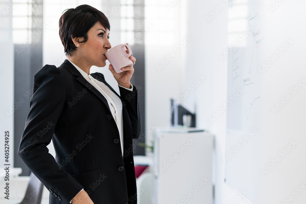 Portrait of businesswoman drinking from mug in front of office whiteboard Portrait of businesswoman drinking from mug in front of office whiteboard