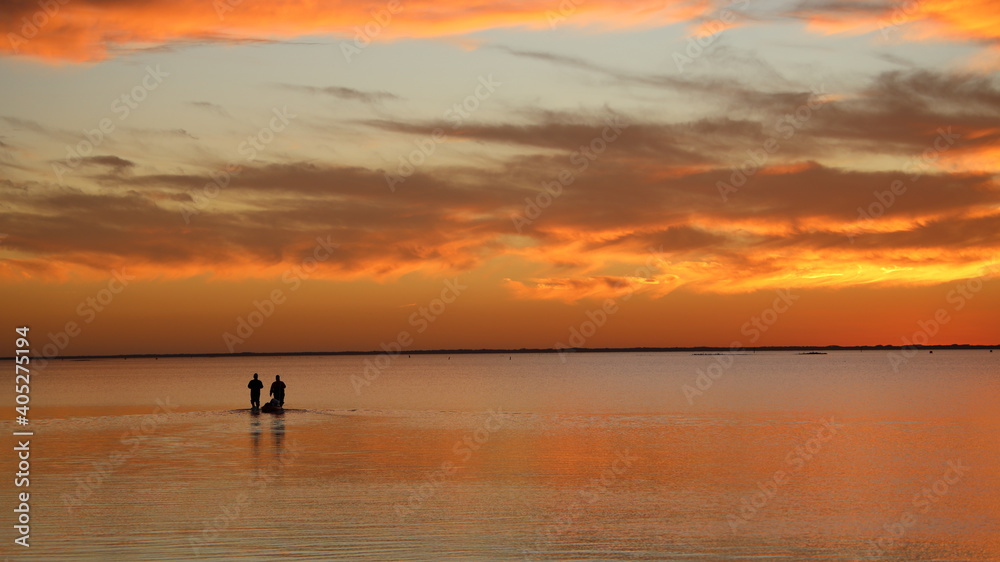 Two people wade in calm water during sensational, colorful sunset at Padre Island, Texas