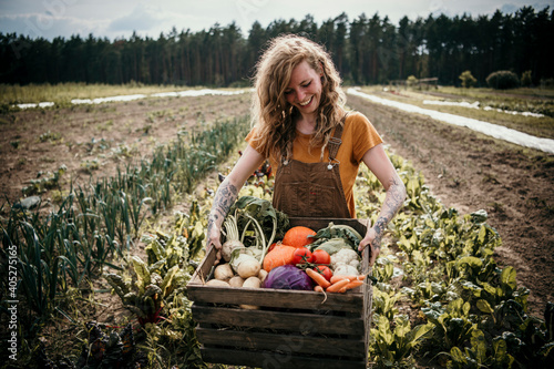 Smiling farm worker carrying vegetable box while standing at farm photo