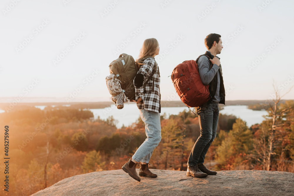 Young couple standing at edge of rocky outcrop admiring surrounding forest at autumn sunset Young couple standing at edge of rocky outcrop admiring surrounding forest at autumn sunset