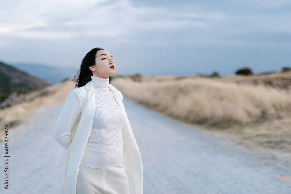 Woman in white jacket standing with hands behind head on road Woman in white jacket standing with hands behind head on road