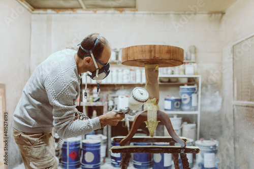 Male carpenter using paint spray gun on table while working at workshop