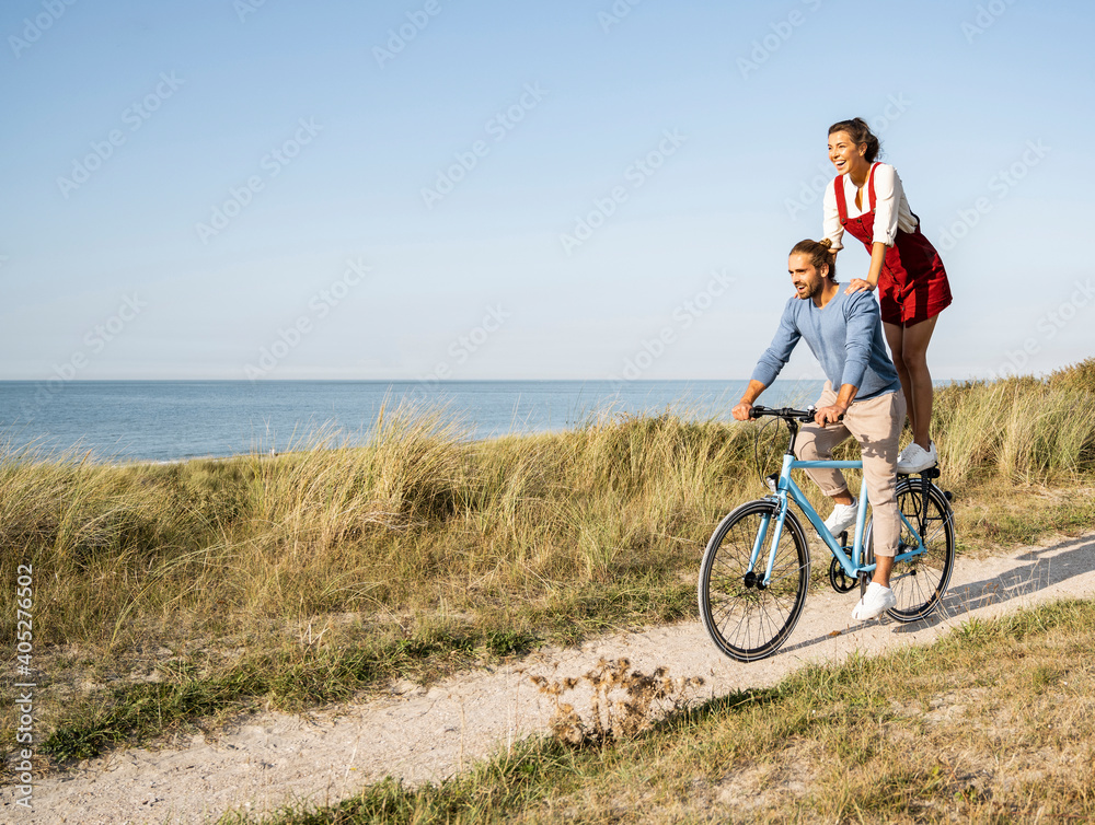 Young woman enjoying ride with man while standing on bicycle against clear sky Young woman enjoying ride with man while standing on bicycle against clear sky