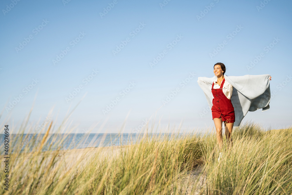 Smiling woman covered in shawl running with arms outstretched against clear sky