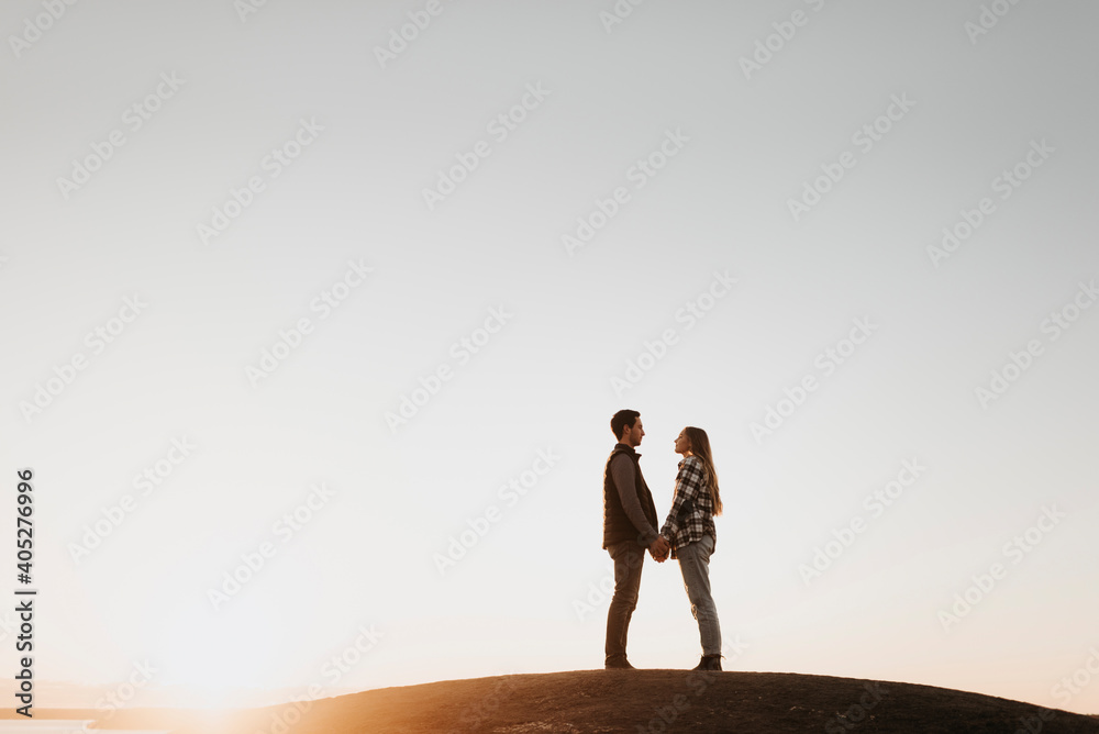 Young couple holding hands against clear sky at sunset