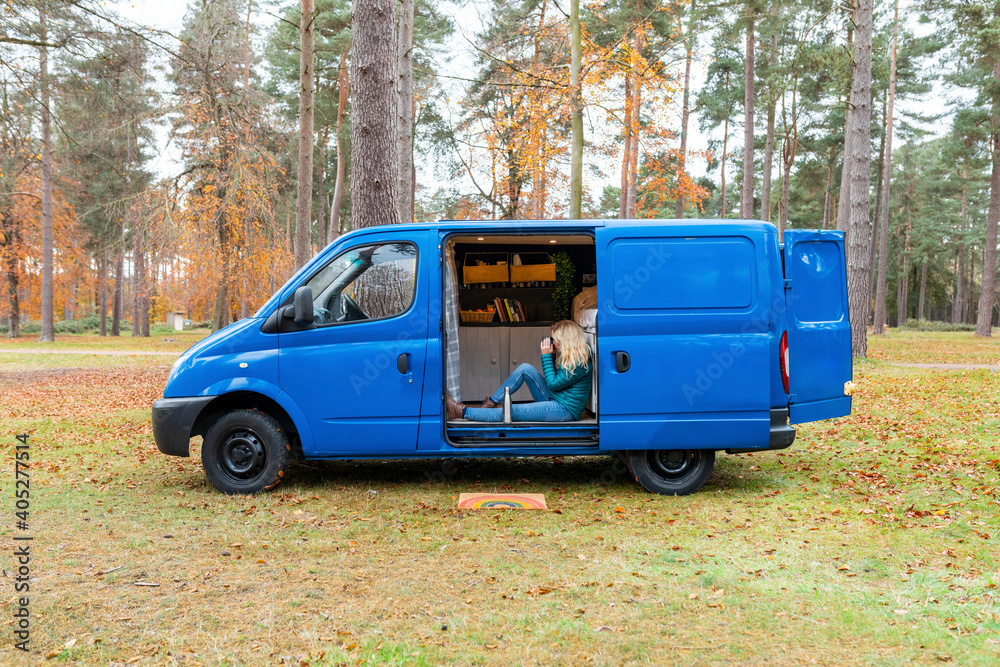 Woman with blond hair drinking tea at door of camper van at Cannock Chase
