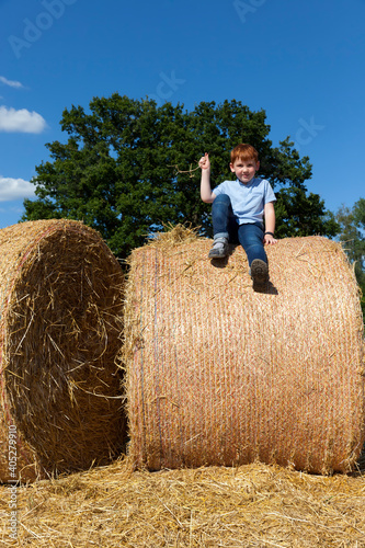 Fotografia, Obraz boy sits on top of a golden straw stack