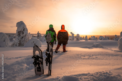 Obraz na plátně Two person looking at the sunset after doing snowshoeing on a snowy and frozen h