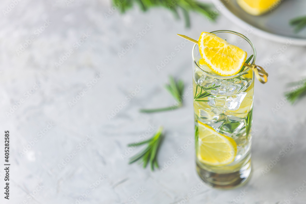 Fototapeta premium Refreshing lemon lime drink with ice cubes in glass goblets against a light gray background. Summer fresh lemon soda cocktail with rosemary, selective focus