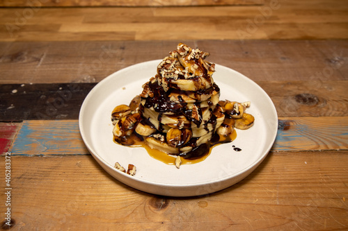 A delicious plate of Banoffee Pecan and Chocolate Pancakes draped in Chocolate and toffee source, on a wooden kitchen table