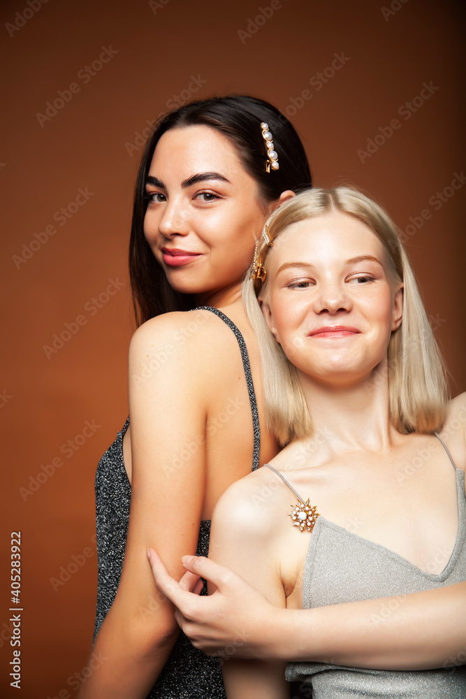 two pretty diverse girls happy posing together: blond and brunette on brown background, lifestyle people concept two pretty diverse girls happy posing together: blond and brunette on brown background, lifestyle people concept