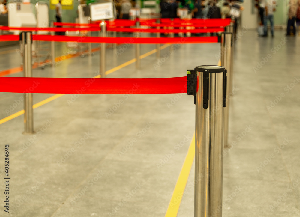 Barriers with red tape on a metal pole at the airport on a blurred background. Check-in counters or ticket sales counters.