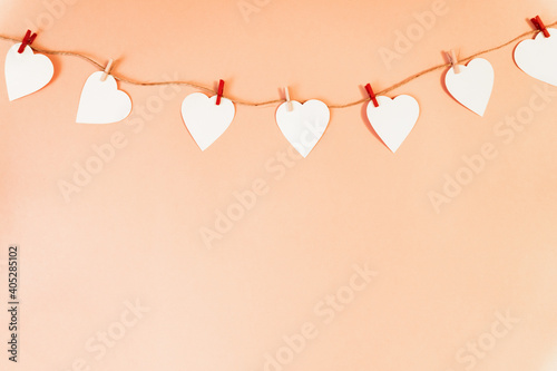 A white paper hearts hanging from a sisal yarn on peachy background.  Greeting card with copy space for your text