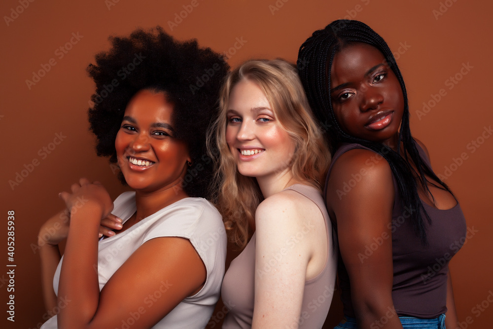 young pretty caucasian, afro, scandinavian woman posing cheerful together on brown background, lifestyle diverse nationality people concept young pretty caucasian, afro, scandinavian woman posing cheerful together on brown background, lifestyle diverse nationality people concept