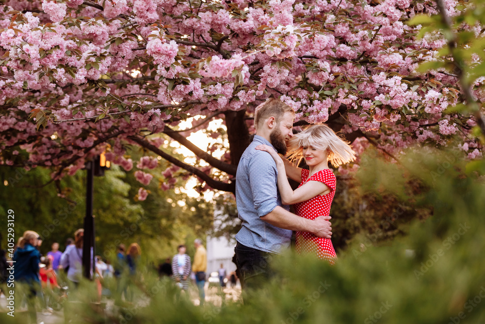 Stylish lovers near the blossoming Sakura. beautiful young couple, man with beard and blonde woman hugging and having fun in the spring park. Concept spring. fashion and beauty