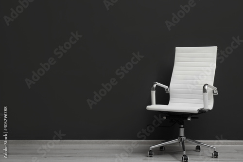 Comfortable office chair near black wall indoors. Space for text photo