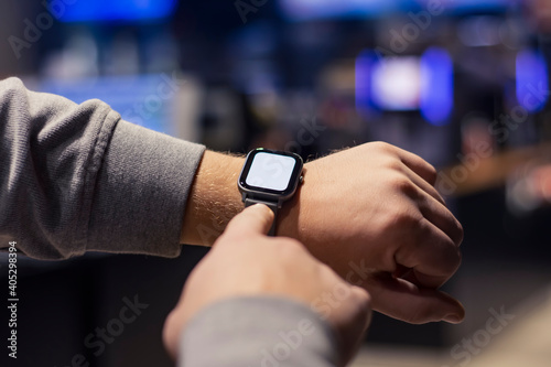 A man with a smartwatch and a white screen mockup on his hand. A man uses a fitness tracker on the background of a shopping mall. © vadish