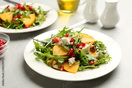 Delicious persimmon salad with pomegranate and arugula served on light grey table