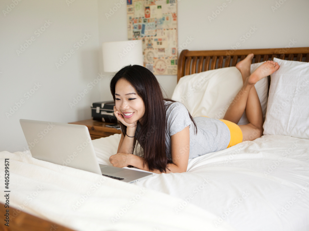 Young woman lying down in bed, using laptop Young woman lying down in bed, using laptop