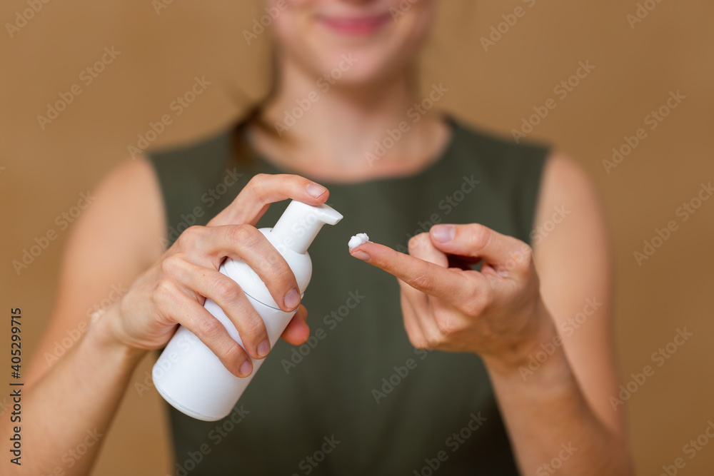 Cheerful young woman applying white cream on her skin and smiling. Skincare and cosmetics concept. Girl pushing moisturizer from a tube on her fingers.