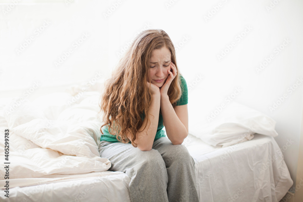 Sad young woman sitting in bed