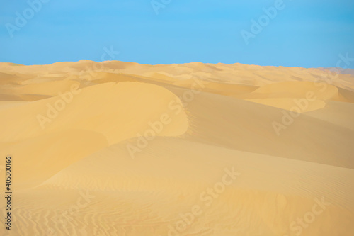 A high-quality horizontal background of a desert with sand dunes and a blue sky. 