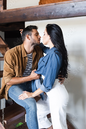 young stylish couple kissing on wooden stairs at home with closed eyes
