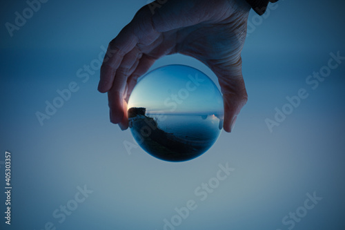 Blue sky with a clear lake in crystal glass ball holding in hand