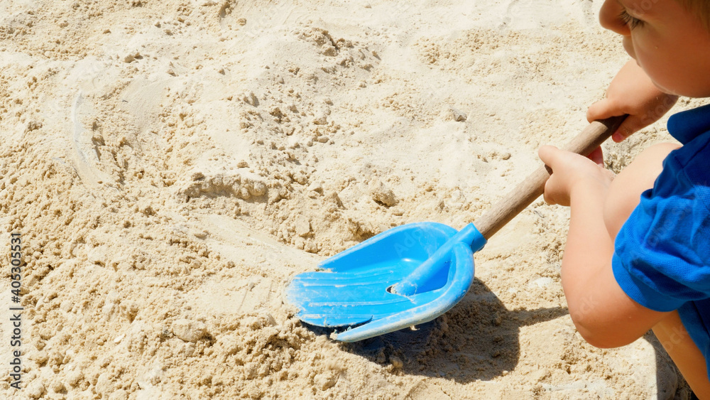 Closeup of little boy digging sand on the playground with plastic scoop or shovel Closeup of little boy digging sand on the playground with plastic scoop or shovel