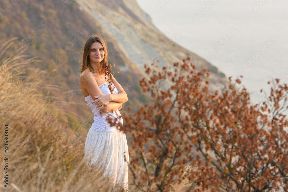 A beautiful girl stands on a rocky seashore and hugs wildflowers