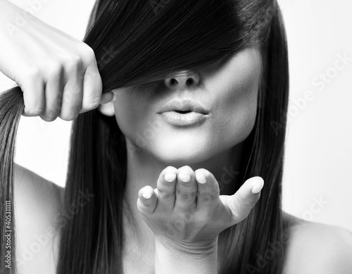 фотографія Portrait of young pretty woman model with silky long straight hair holding strand and sending air kiss over white background