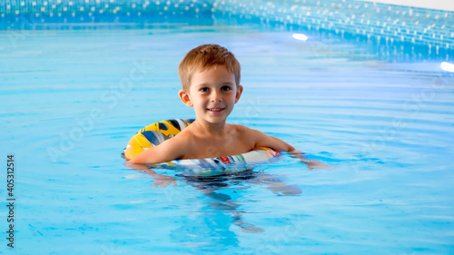 Happy cheerful little boy using inflatable ring while learning swimming in indoor swimming pool at hotel.