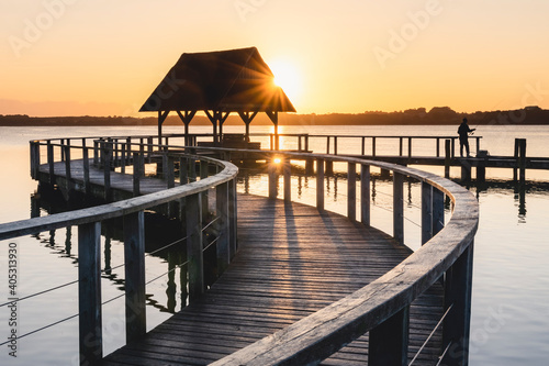 Germany, Schleswig-Holstein, Hemmelsdorf, Sun rising over pier on shore of Hemmelsdorfer See lake photo