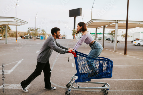 Boyfriend pushing girlfriend standing in shopping cart on road photo